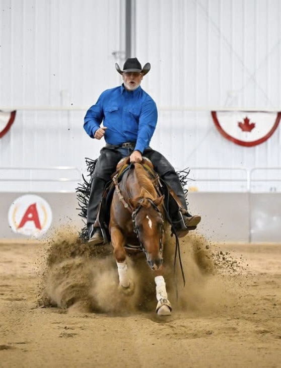 Mike riding a chestnut horse in a hard sliding stop, blue shirt and black chaps